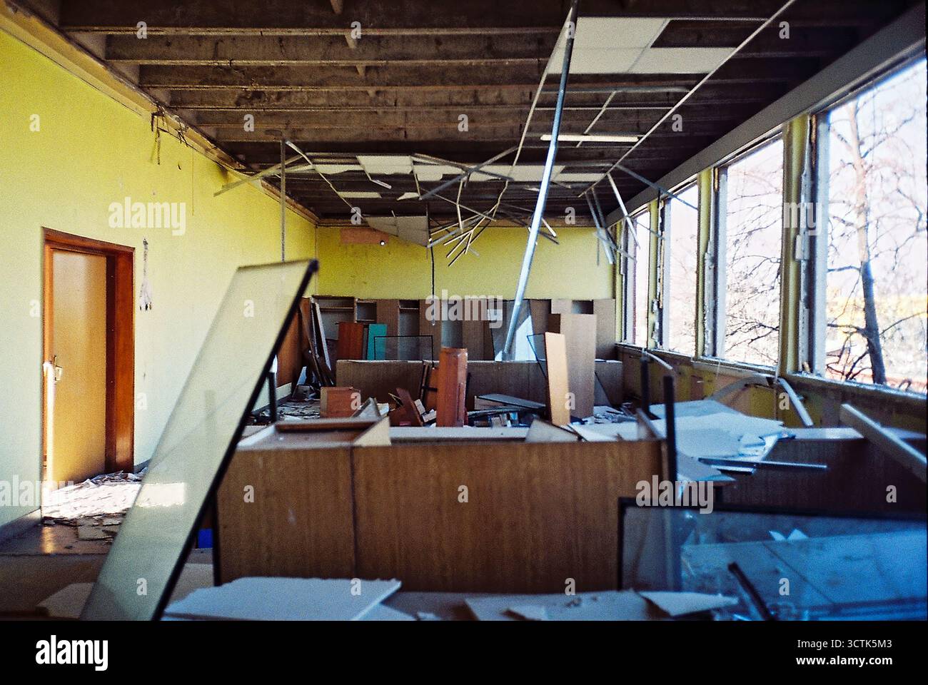Bureau dans une usine abandonnée en cours de démolition, remplie de débris et de vieux meubles, avec des fenêtres manquantes, capturées sur film analogique. Banque D'Images