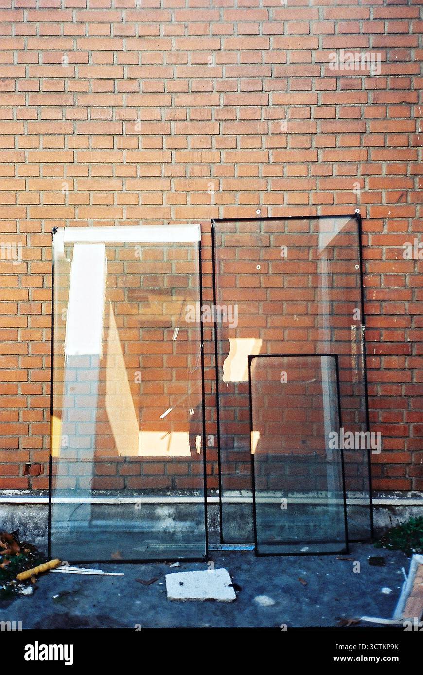 Verre d'une fenêtre enlevée appuyée contre un mur de briques rouges, reflétant le photographe. Film analogique. Banque D'Images
