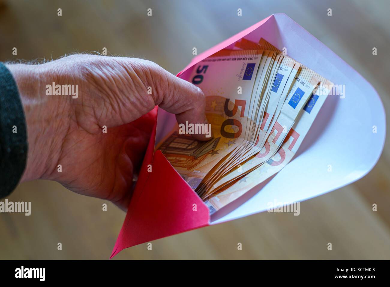 Gros plan d’une main tenant une enveloppe remplie de billets de 50 euros, symbolisant épargne, salaire, pension, aide financière, paiement en espèces ou cadeau Banque D'Images