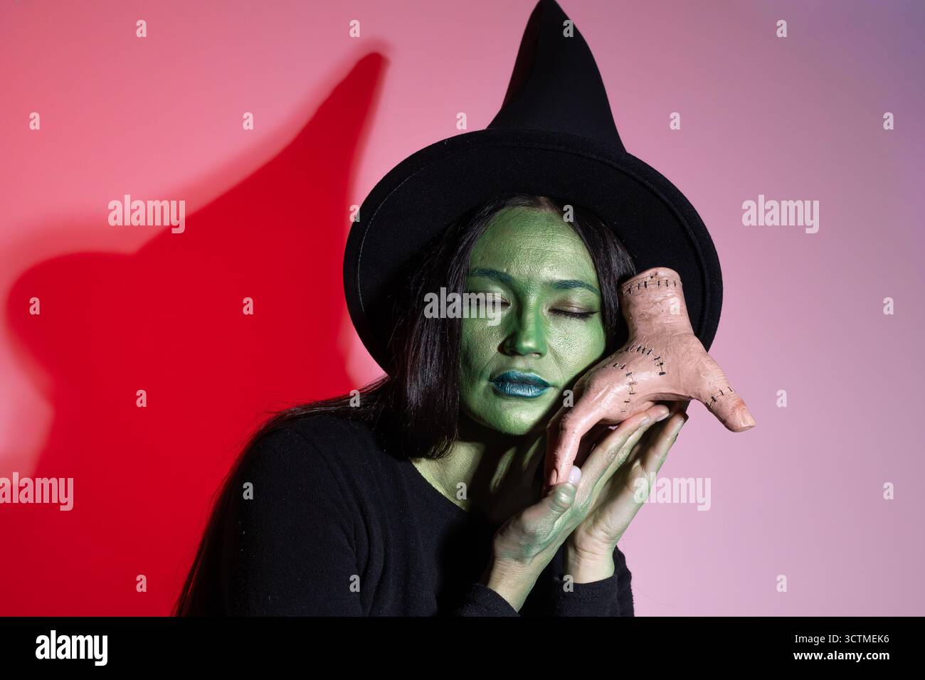 Une femme au maquillage vert et un chapeau de sorcière debout devant un chaudron Banque D'Images
