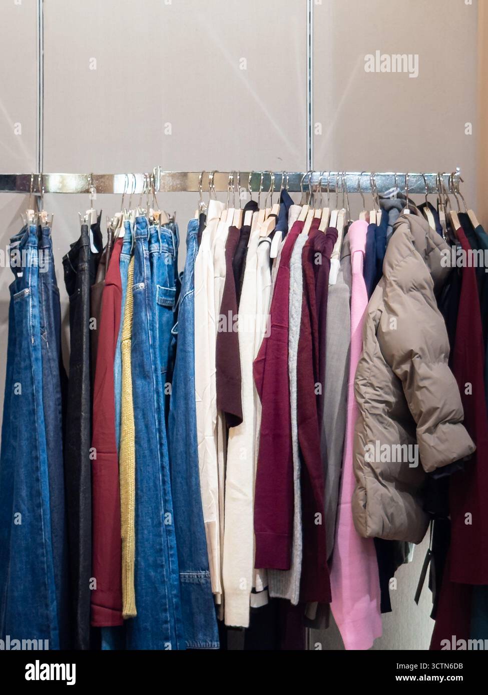 Gamme diversifiée d'articles de mode modernes d'automne et d'hiver sur un support de vente au détail. Présente les tendances actuelles en matière de vêtements décontractés, y compris le denim et les vêtements d'extérieur pour la saison. Photo verticale. Banque D'Images
