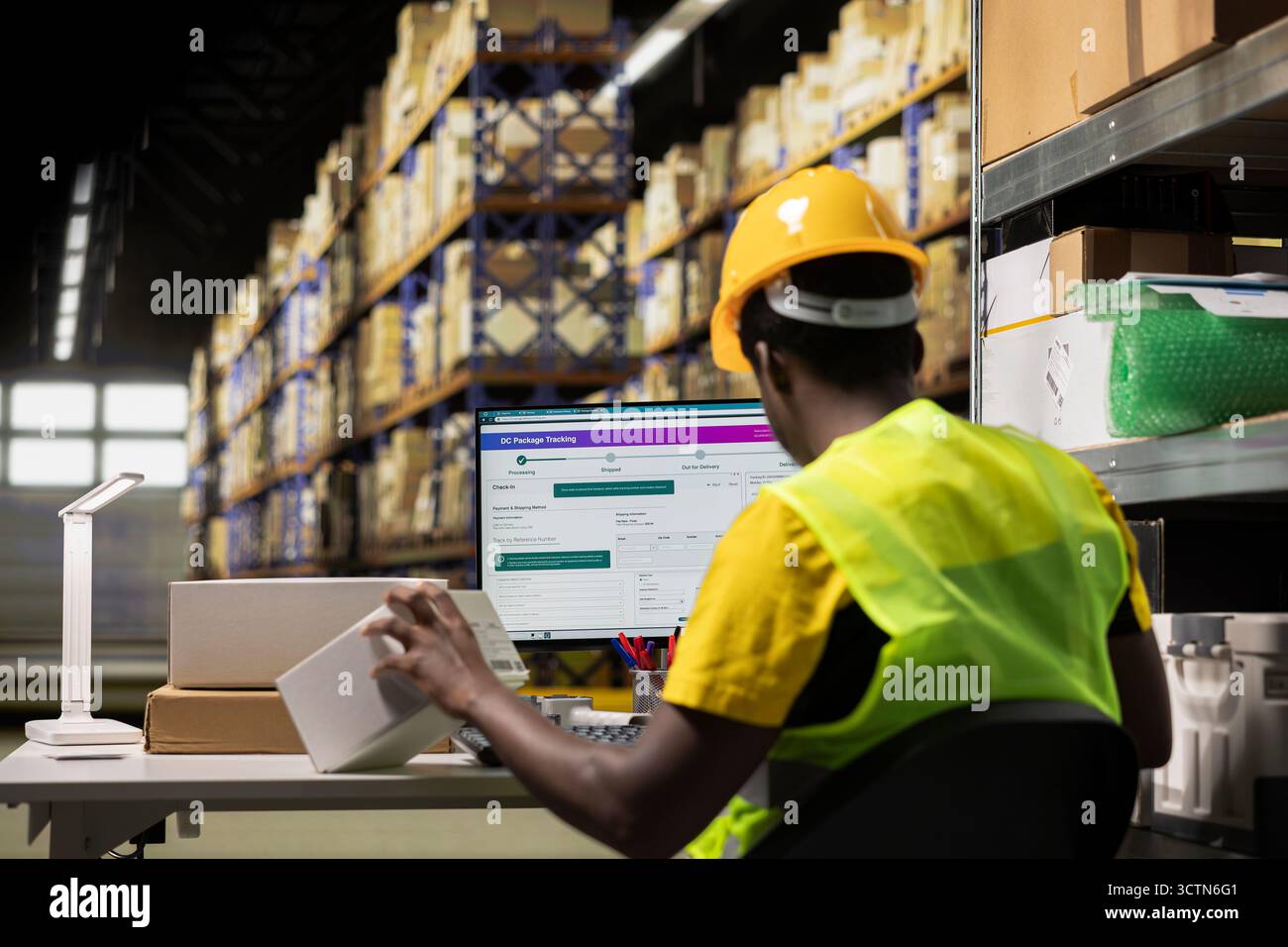 Homme afro-américain vérifiant les détails de l'expédition sur les étiquettes awb, examinant les boîtes en carton pour assurer une distribution transparente des palettes à partir de l'espace d'entrepôt. Personnel avec gilet haute visibilité et casque. Banque D'Images