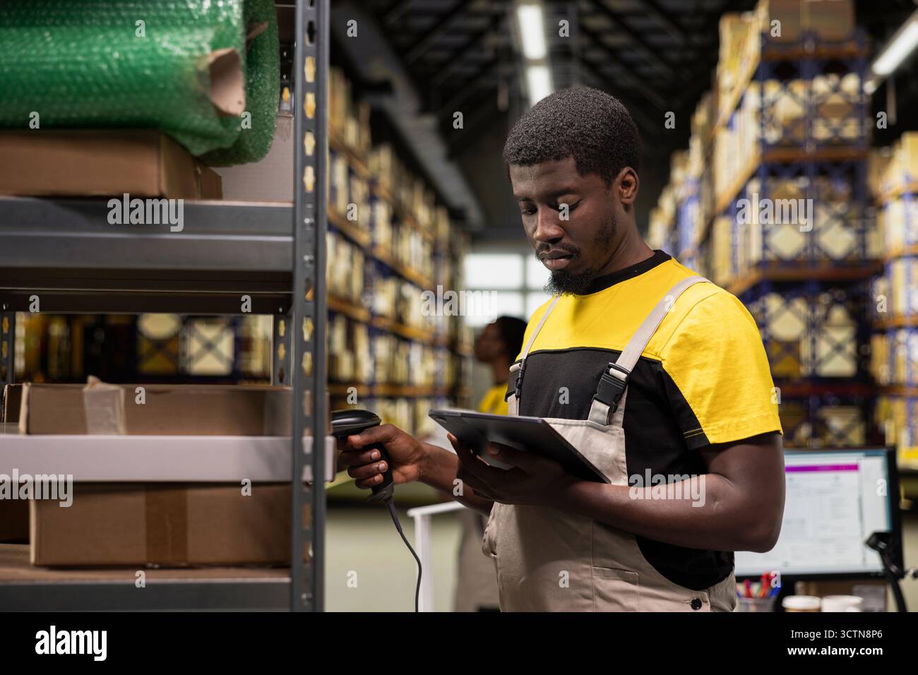 Travailleur logistique afro-américain saisissant les détails des factures de transport aérien et scannant les étiquettes sur les boîtes. Le suivi des colis, les étiquettes awb et les enregistrements rationalisent les opérations d'expédition dans un environnement commercial de grande taille. Banque D'Images