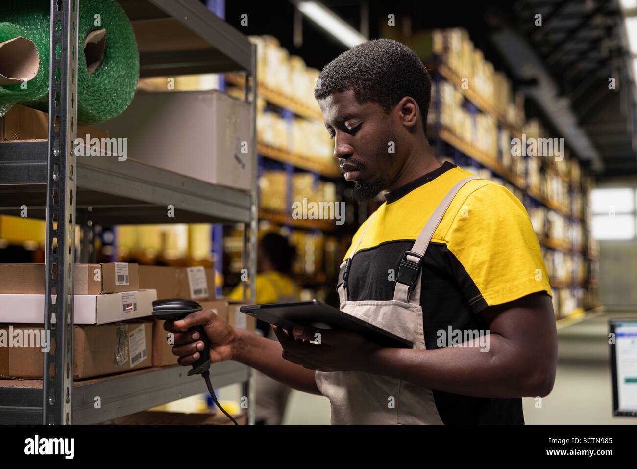 Homme afro-américain utilisant un scanner de codes-barres pour traiter les étiquettes d'expédition sur les boîtes des racks de stockage industriels. Scanner les étiquettes awb pour le service de suivi des colis avec des informations de suivi, une logistique précise. Banque D'Images
