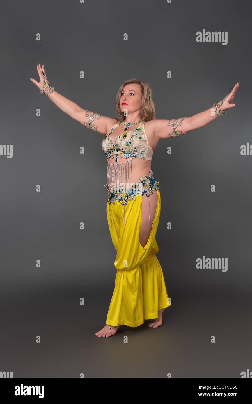 Danseuse femme adulte d'âge moyen avec les bras tendus vêtus dans la tenue de danse - haut et pantalon de harem jaune et elle ne porte pas de chaussures, mouvement Banque D'Images