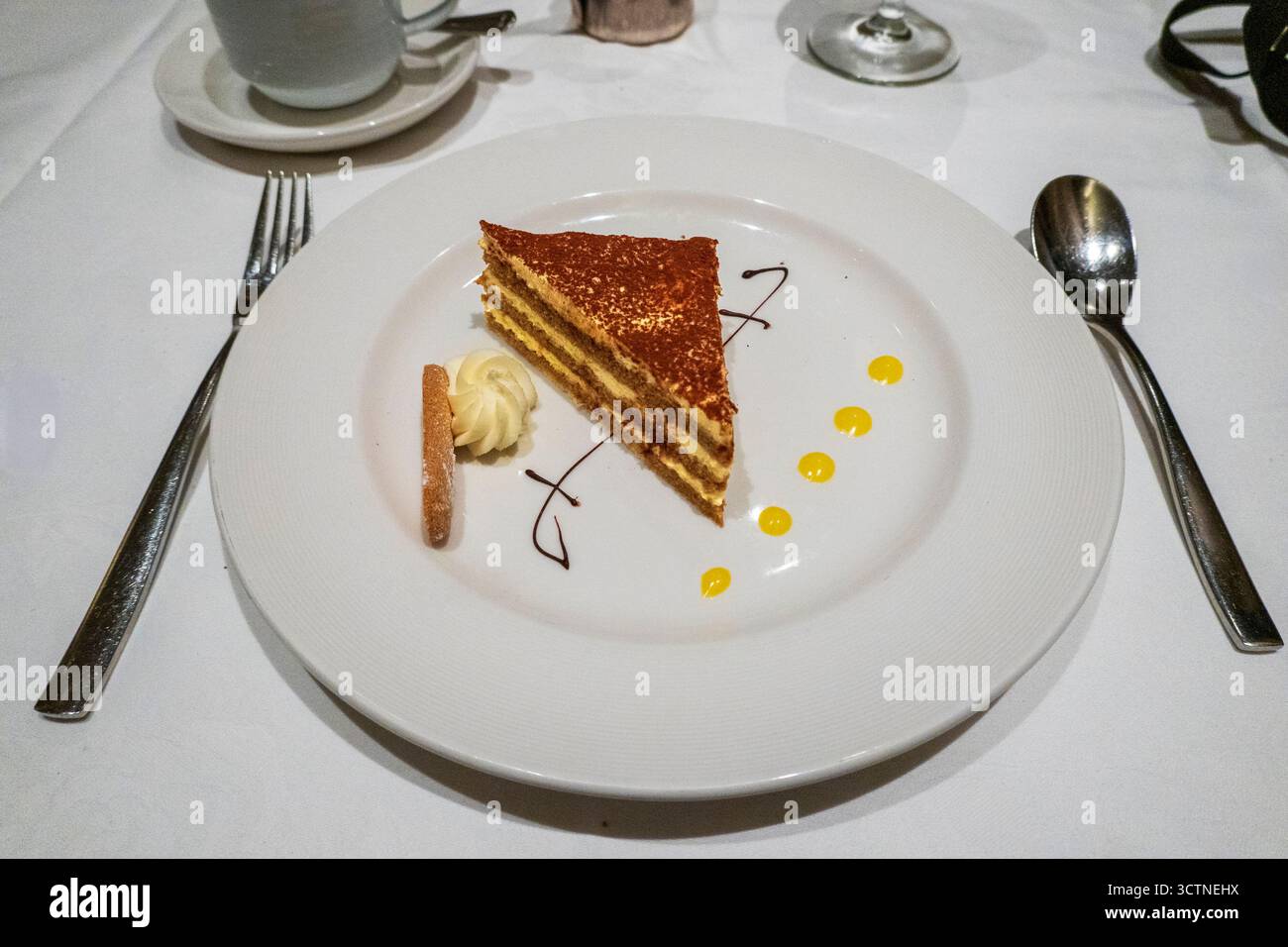 Une élégante tranche de gâteau Opéra classique composée de délicates couches de biscuit trempé dans le café, de ganache et de crème au beurre, saupoudrée de poudre de cacao et d'œuvres d'art Banque D'Images