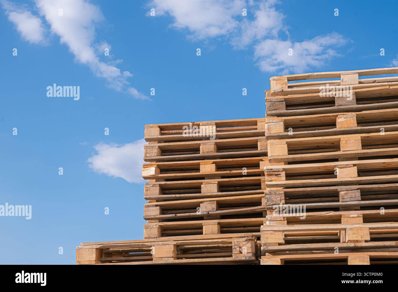 Palettes en bois empilées contre le ciel bleu. Grande pile de palettes en bois disposées de manière ordonnée. Concept lié à la logistique ou à l'entreposage. Banque D'Images