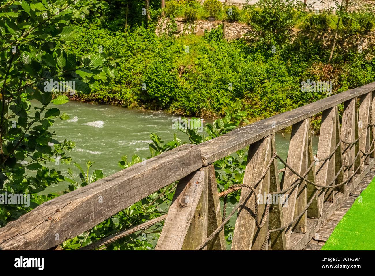Pont en bois rustique sur la rivière ruisselante dans une verdure luxuriante. Vue rapprochée d'un pont en bois avec des détails de corde le long de sa balustrade. L'image est appropriée Banque D'Images Pont en bois rustique sur la rivière ruisselante dans une verdure luxuriante. Vue rapprochée d'un pont en bois avec des détails de corde le long de sa balustrade. L'image est appropriée Banque D'Images