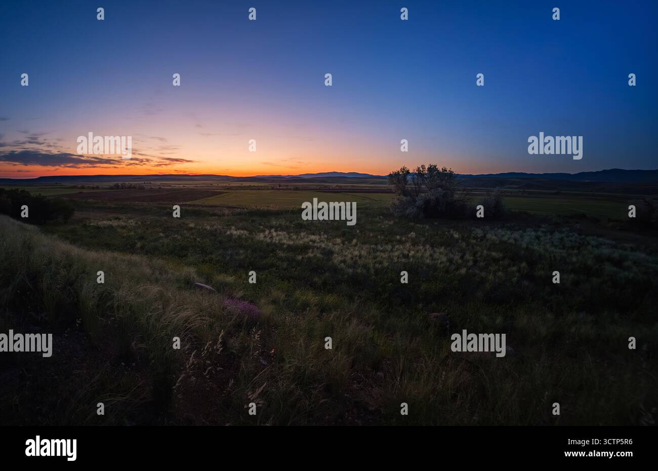 Prise de vue panoramique grand angle capturant la transition sereine du jour à la nuit sur un vaste paysage rural. Champs et montagnes lointaines silhouettent agai Banque D'Images
