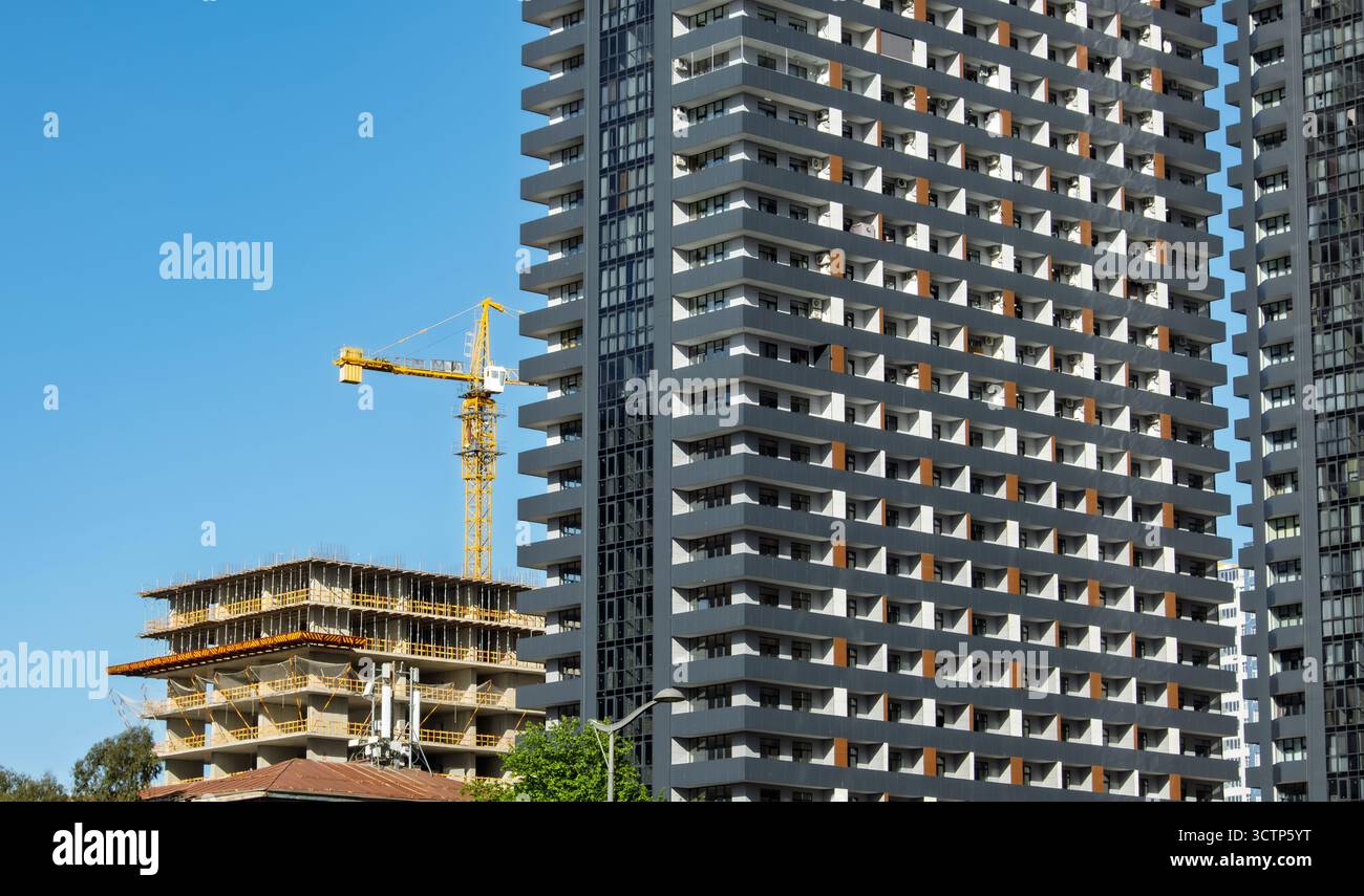 Immeuble de grande hauteur et grue à tour contre le ciel bleu. Photographie de paysage urbain capturant un bâtiment moderne à côté d'une structure en construction avec remorquage Banque D'Images