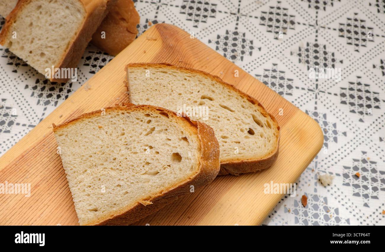 Pain rustique tranché sur planche à découper en bois. Pain fraîchement tranché placé sur une nappe à motifs. Parfait pour le petit déjeuner ou des collations. Mise au point sélective Banque D'Images