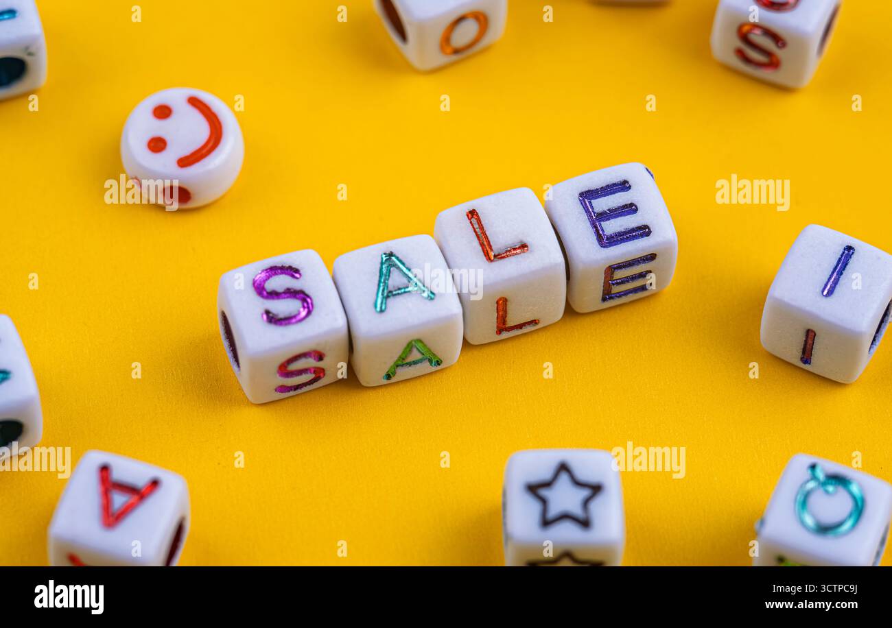Les perles de lettres blanches orthographiant 'SALE' en lettres colorées sont bien en évidence affichées sur fond jaune. Entouré de perles dispersées. Y compris un smil Banque D'Images