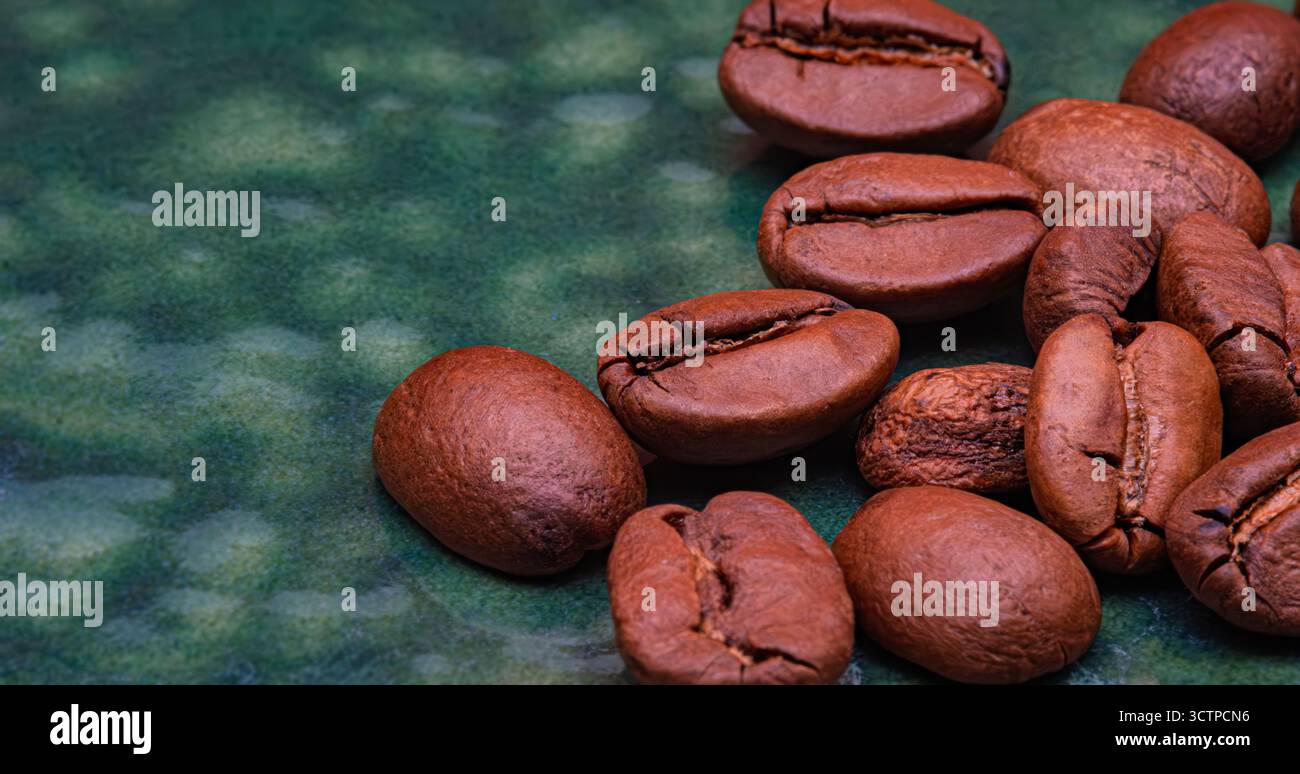 Gros plan de grains de café torréfiés sur une surface texturée verte. Les tons bruns riches soulignent l'arôme, la saveur et la texture. Symbolisant la chaleur, l'énergie et Banque D'Images