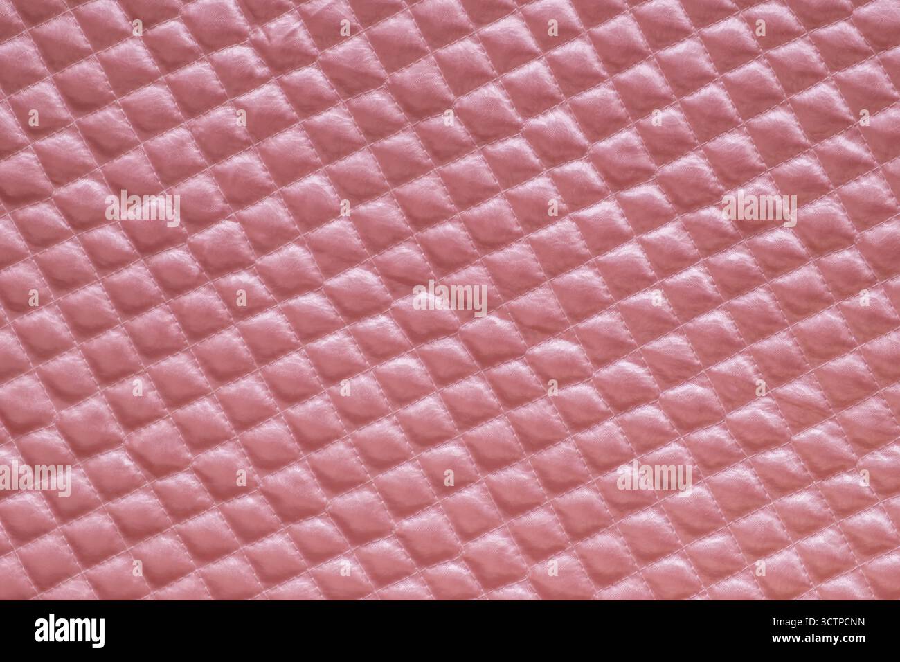 Gros plan de tissu matelassé rose doux avec un motif de losanges. Mettant en valeur sa texture pelucheuse et son éclat subtil. Idéal pour les arrière-plans ou les dessins textiles. Banque D'Images