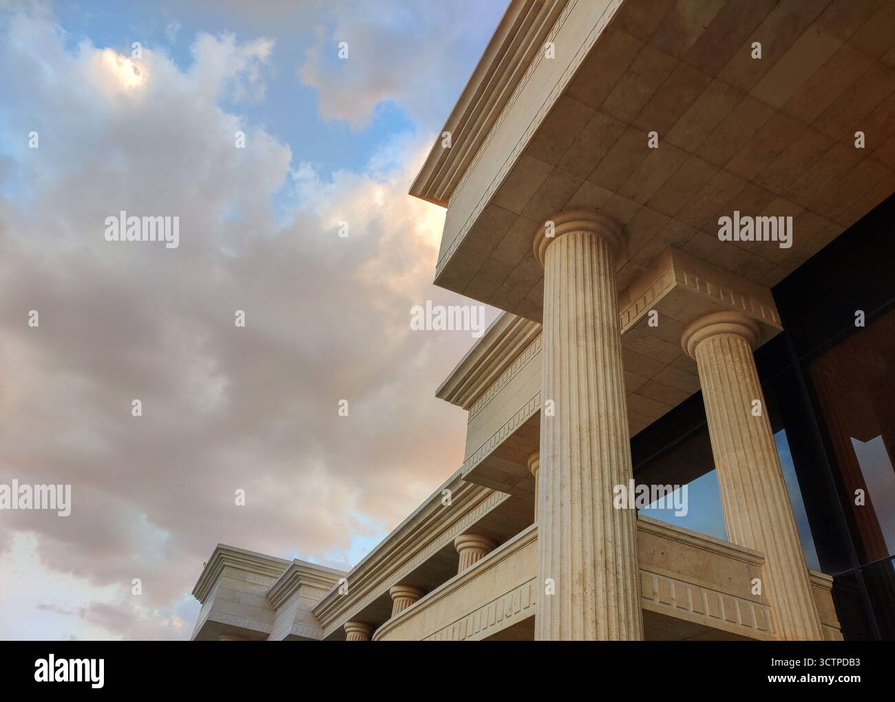 Vue en bas angle d'un bâtiment néoclassique avec de hautes colonnes de pierre et des chapiteaux détaillés contre un ciel nuageux. L'architecture met l'accent sur la force. Banque D'Images