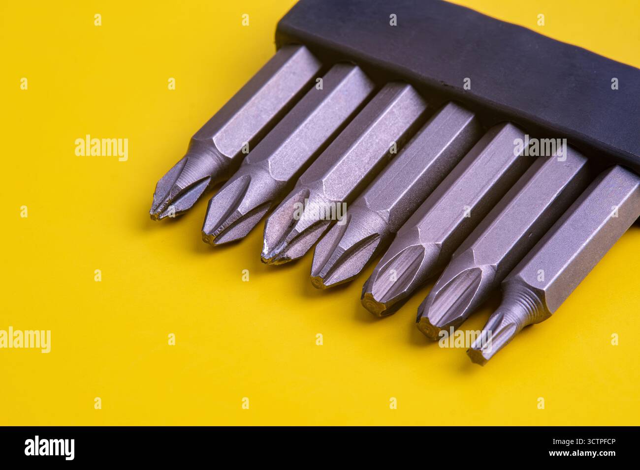 Les embouts de tournevis métalliques, y compris les embouts Phillips et Torx, sont soigneusement disposés dans un support noir sur fond jaune vif. Banque D'Images