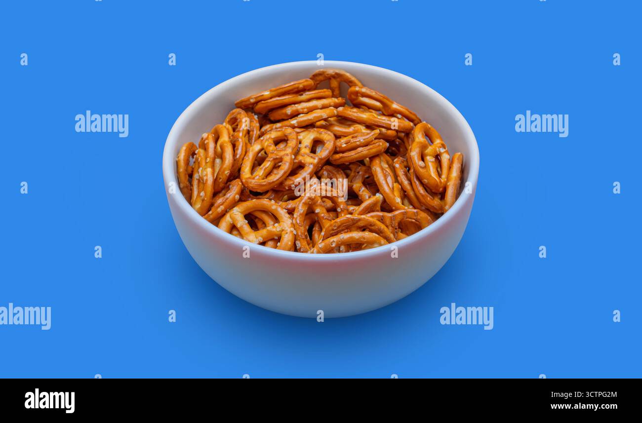 Bol blanc rempli de bretzels salés croustillants sur un fond bleu Uni. Les collations au bretzel brun doré se démarquent. Mise en surbrillance de la texture. Banque D'Images