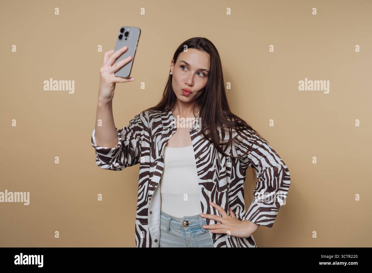 Femme prenant un selfie avec un smartphone sur fond beige. Banque D'Images
