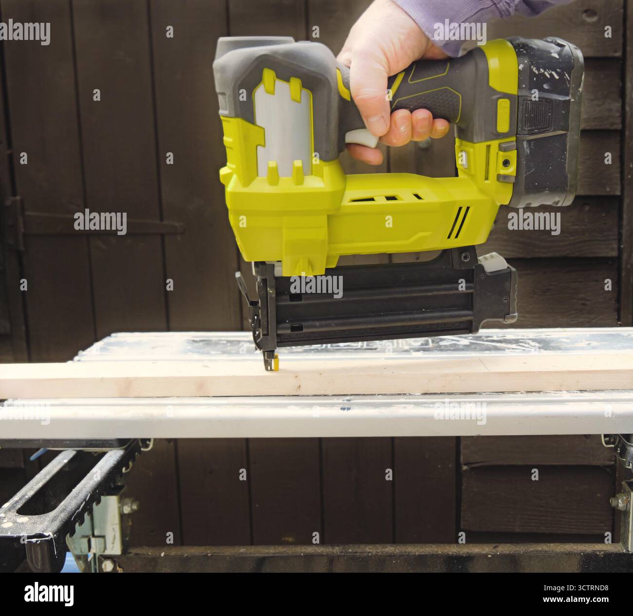 L'ouvrier pousse des clous dans la poutre en bois à l'aide d'un pistolet à clous alimenté par batterie sur le chantier sous le jour des travaux Banque D'Images