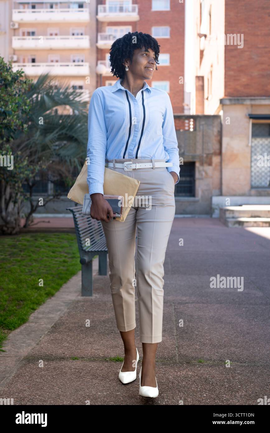 Femme noire confiante en tenue décontractée d'affaires marchant à l'extérieur dans un cadre urbain Banque D'Images