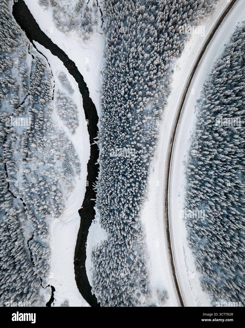 Vue aérienne d'une rivière sombre serpentant à travers un paysage enneigé, bordée d'arbres givrés et d'une route sinueuse, Banff, Alberta, Canada. Banque D'Images