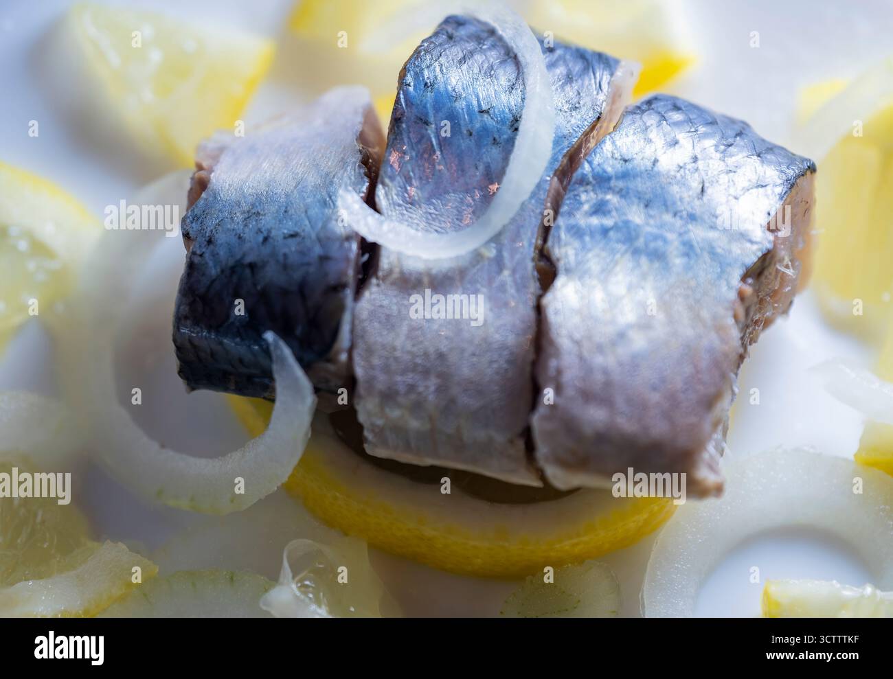 Hareng du Pacifique tranché sur assiette blanche avec jus de citron, rondelles d'oignon et tranches de citron, plat de fruits de mer gros plan Banque D'Images