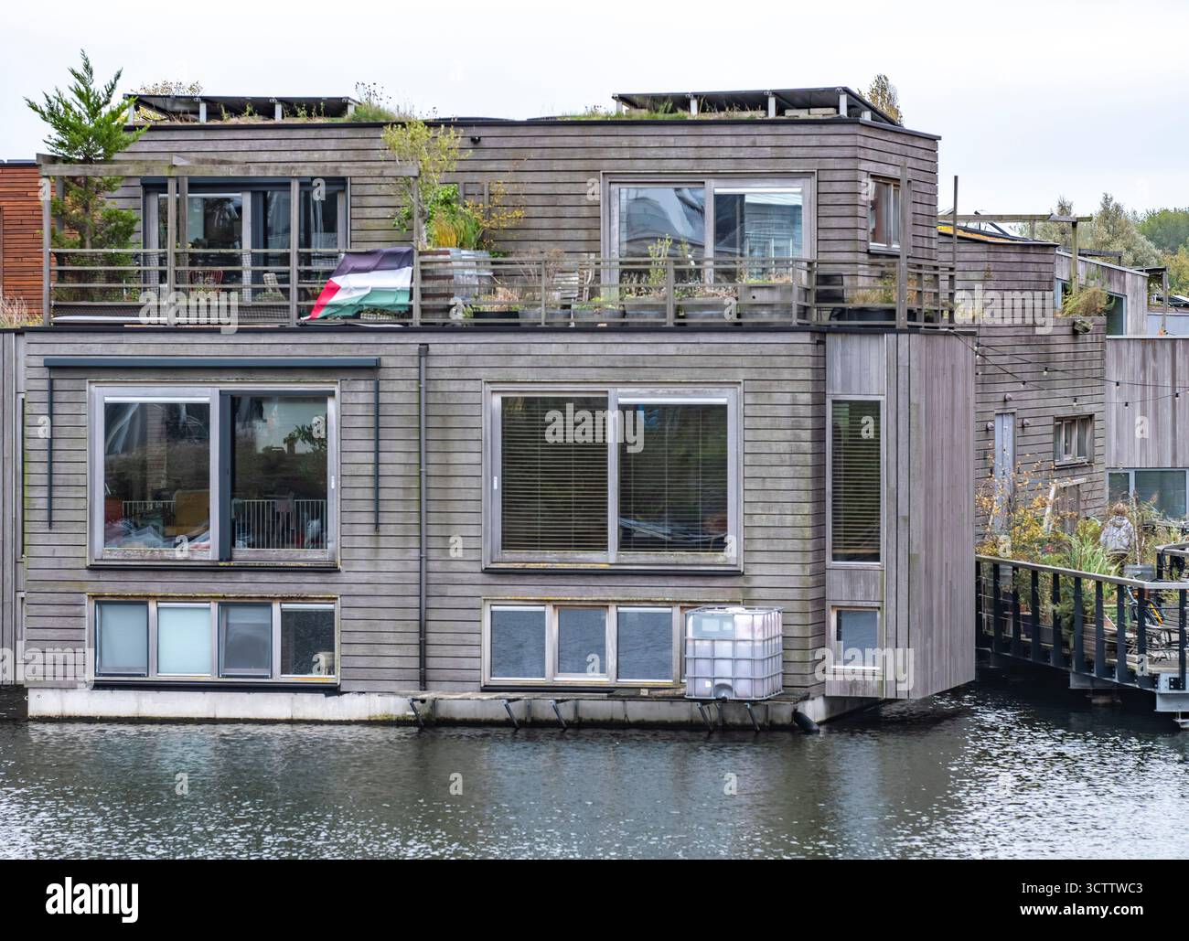 Amsterdam vue sur le canal avec maison sur l'eau et petit bateau sur la gauche, gratte-ciel en construction et bâtiments résidentiels parmi les arbres sur la plate-forme Banque D'Images