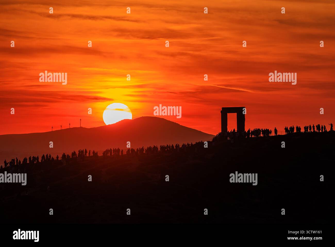 les foules entourent portara à naxos le cadre de porte grec antique silhouetté contre le ciel nuageux orange alors que le soleil se couche derrière la colline en arrière-plan Banque D'Images