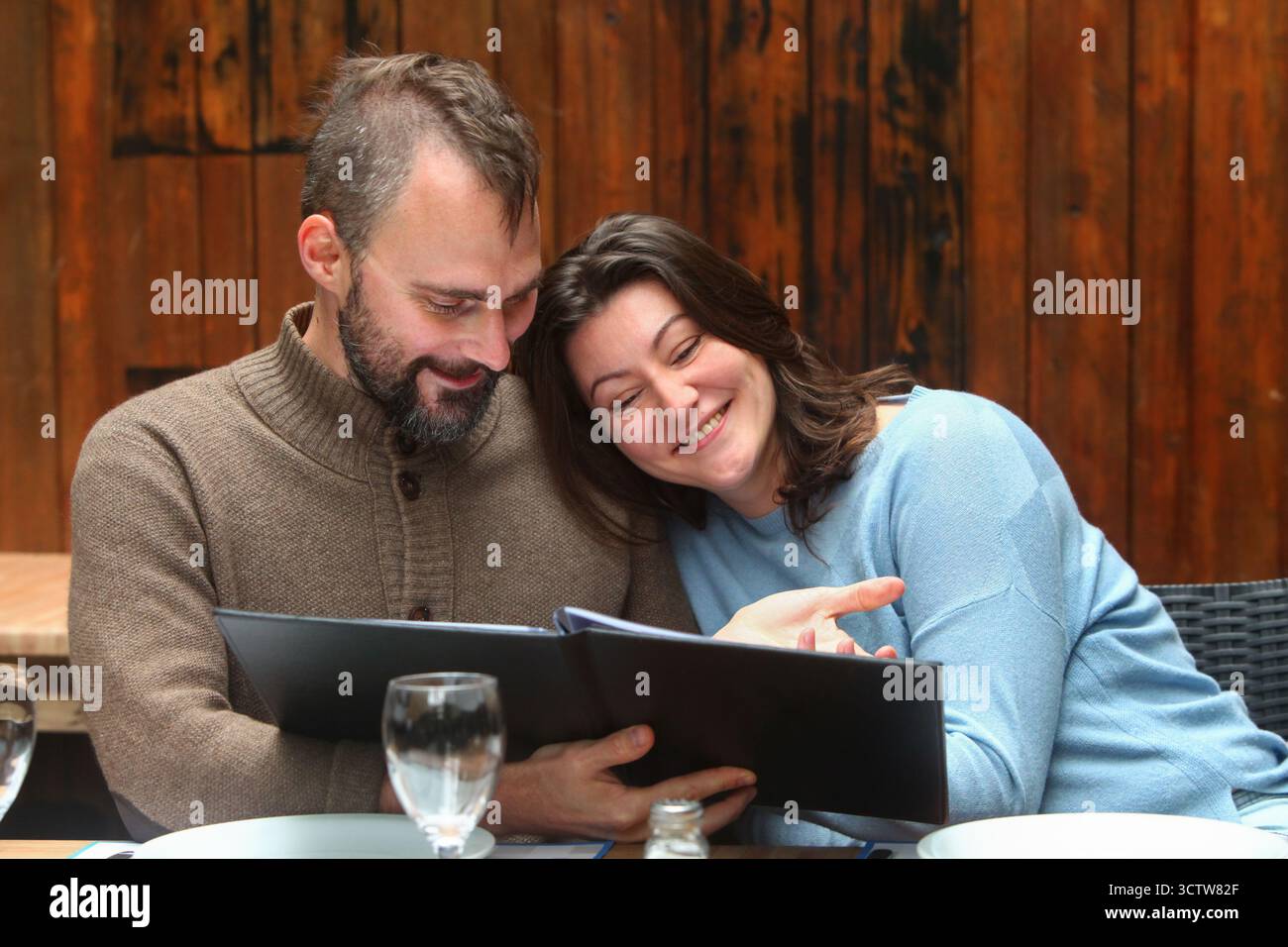Joyeux couple d'âge moyen assis dans un restaurant rustique, regardant le menu et profitant du temps ensemble. Banque D'Images