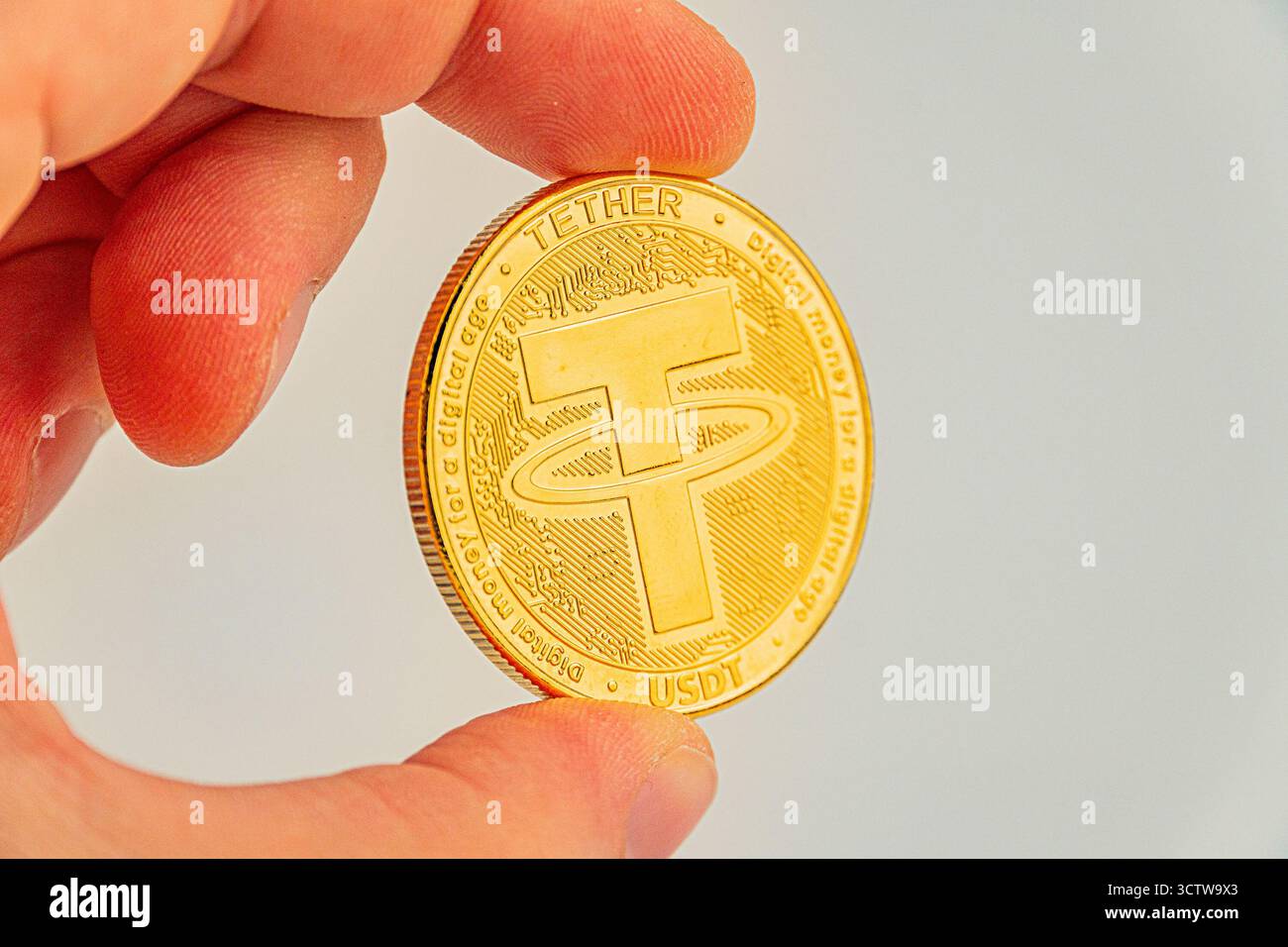 Image en gros plan d'une pièce de monnaie Tether tenue par une main, présentant le symbole B et un dessin en relief peut être utilisé dans des documents de marketing pour la crypto-monnaie, Banque D'Images