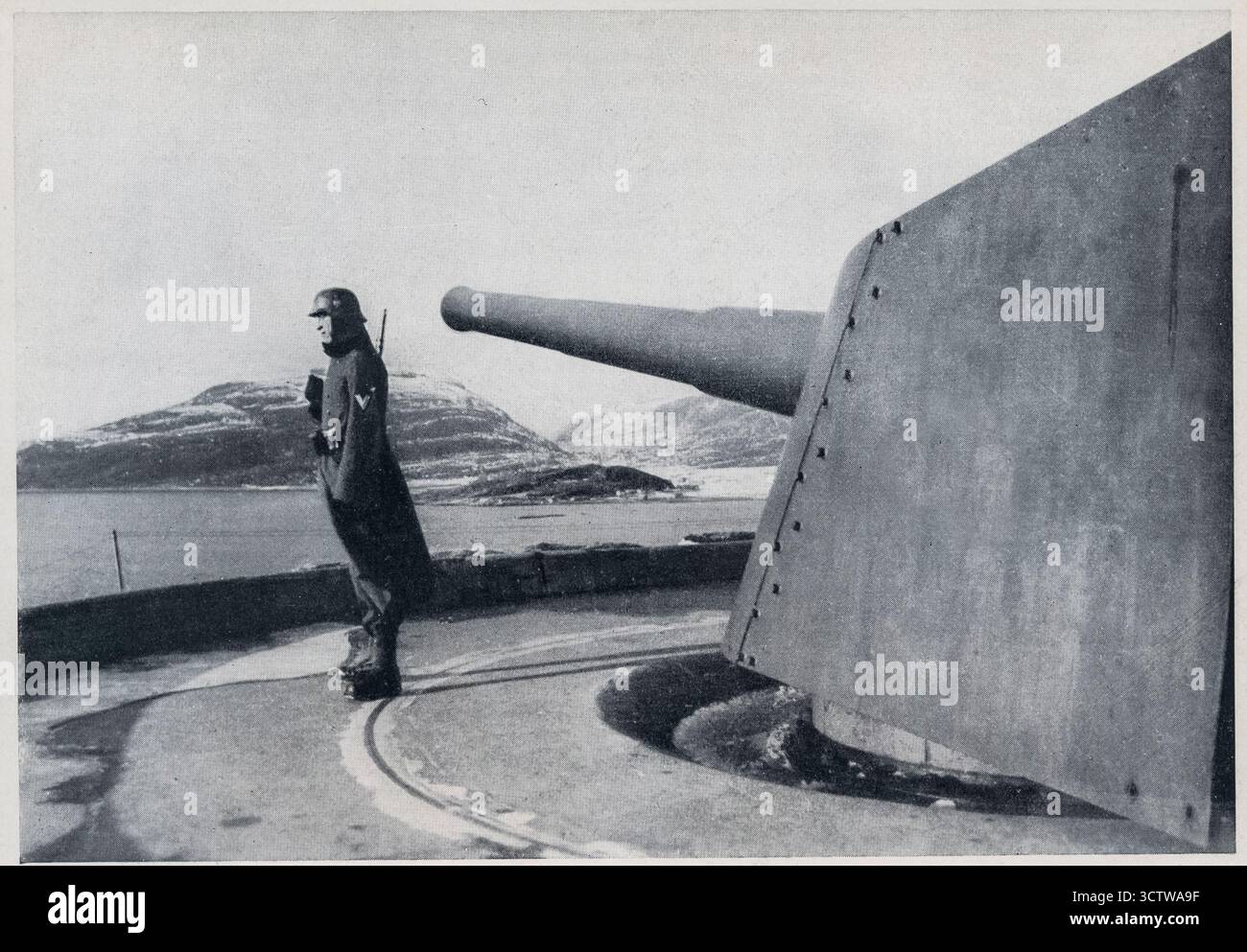 Canon d'artillerie côtière allemand avec un soldat de la Wehrmacht en service au mur de l'Atlantique de l'Allemagne nazie pendant la seconde Guerre mondiale le mur de l'Atlantique était un vaste système de fortifications côtières construit par l'Allemagne pendant la seconde Guerre mondiale pour se défendre contre une invasion alliée de l'Europe. La photo montre un soldat allemand debout à côté d'un canon côtier de gros calibre. Le mur de l'Atlantique s'étendait de la frontière espagnole à la Norvège. Les fortifications comprenaient des batteries d'armes, des bunkers et des obstacles sur les plages. Banque D'Images