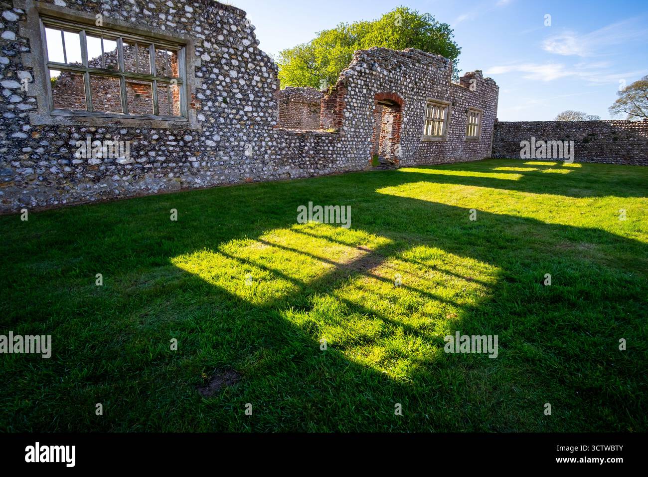 Vue à l'intérieur des ruines de pierre du château de Baconsthorpe avec la lumière du soleil qui coule à travers les fenêtres vides, projetant de fortes ombres sur la cour d'herbe Banque D'Images