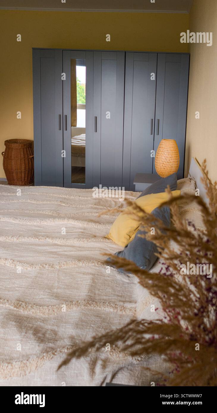 L'intérieur moderne de la chambre comprend un lit, une armoire grise et des accents décoratifs chaleureux. La composition transmet confort et minimalisme dans une lumière douce. Banque D'Images
