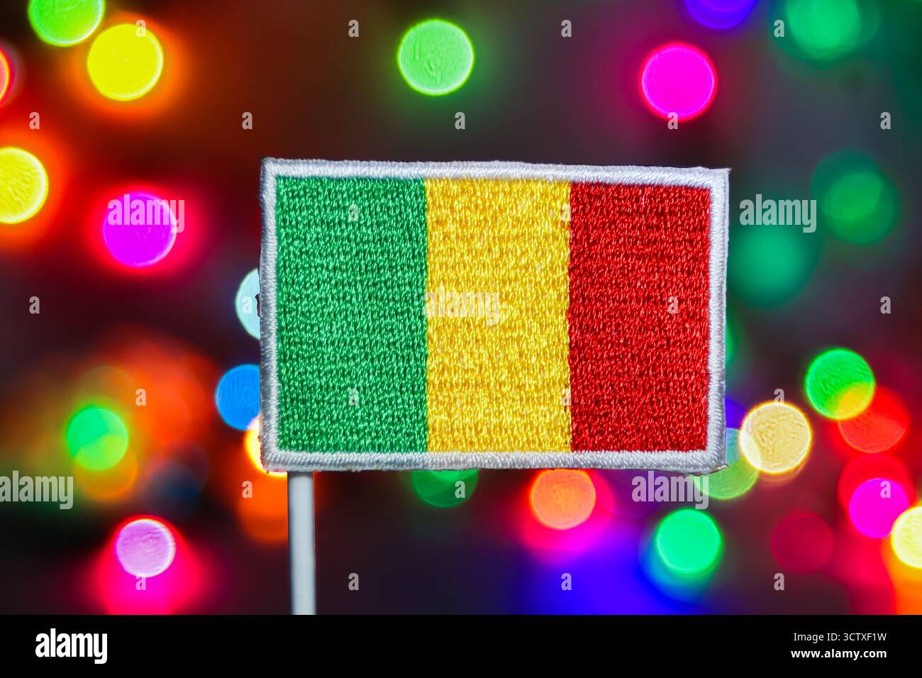 Gros plan d'un drapeau du Mali brodé détaillé, placé sur un bokeh multicolore à flou doux idéal pour les célébrations nationales et les thèmes du nouvel an. Banque D'Images