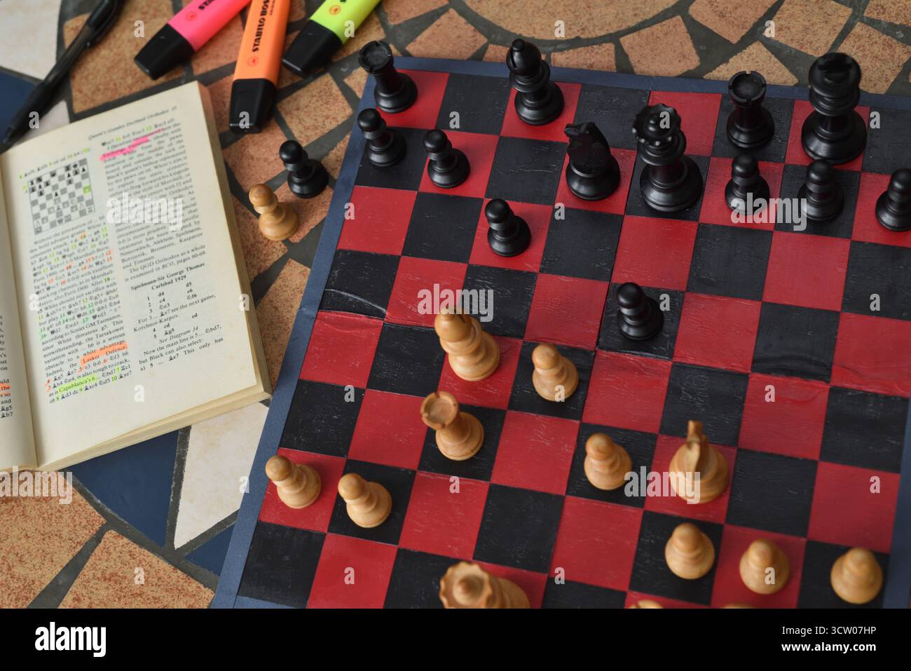 Apprendre l'ouverture des échecs Queens Gambit à l'aide d'un livre d'échecs et d'un jeu d'échecs vintage avec des échiquiers Staunton en bois de buis sur un tableau rouge et noir Banque D'Images