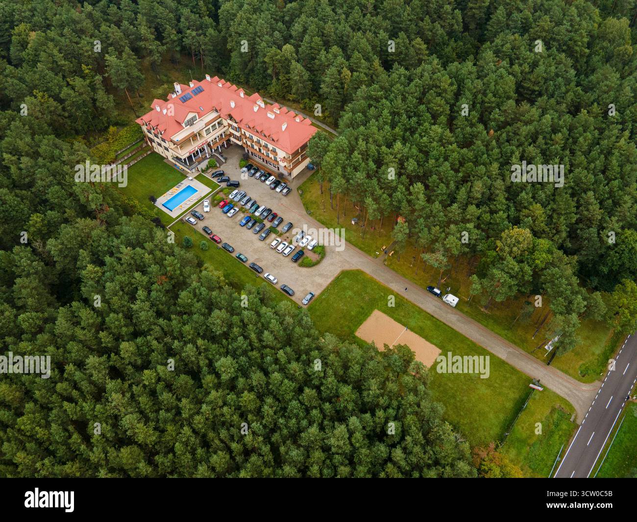 Prise de vue aérienne de l'hôtel Drohicki par drone, montrant l'architecture détaillée du toit et un parking organisé entouré d'une forêt dense Banque D'Images