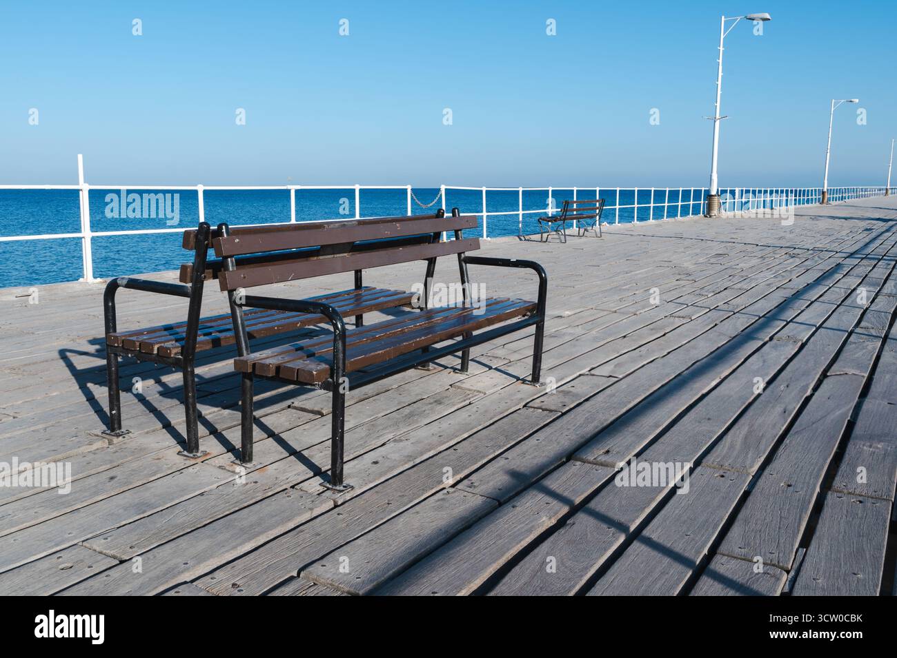 Une vue sereine sur un banc en bois rustique sur une jetée, surplombant les eaux bleues calmes et le ciel clair dans un paysage idyllique Banque D'Images