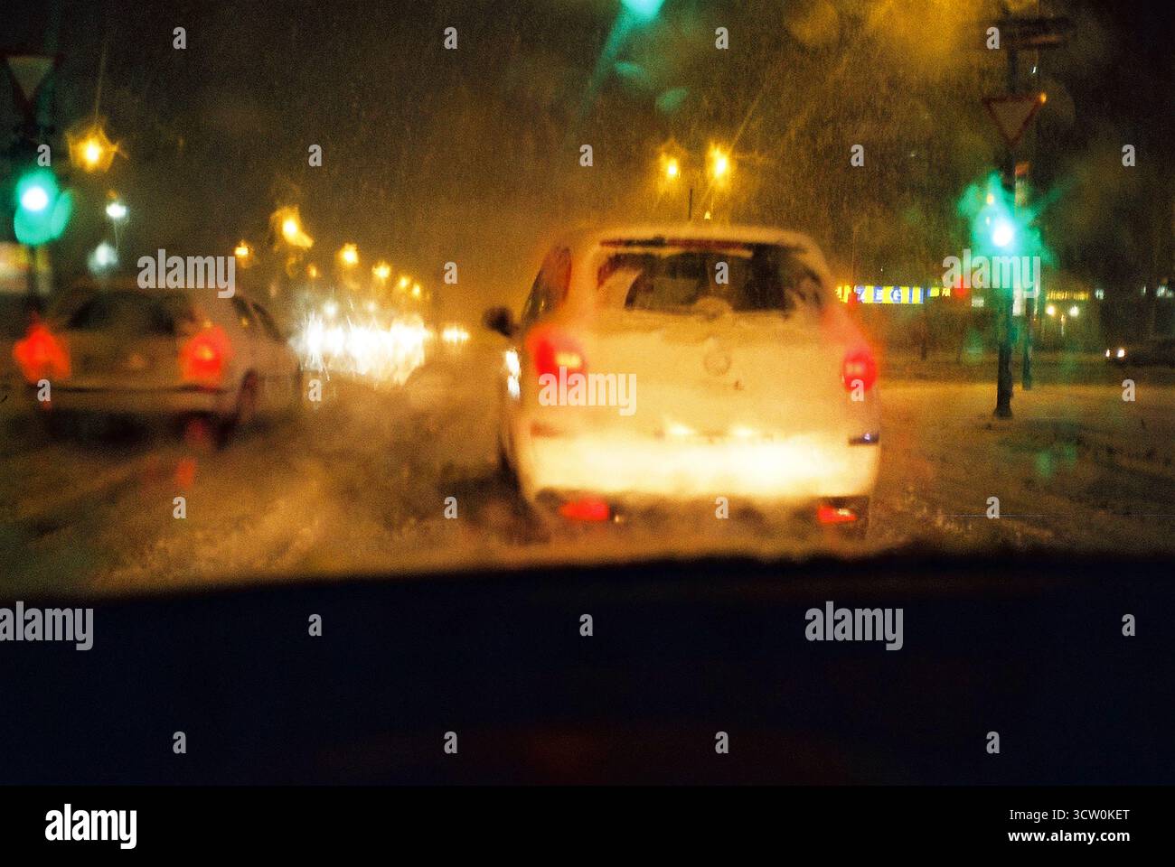 Photo analogique du pare-brise embué POV à un feu vert. La neige brouille les voitures et les lumières dans une scène hivernale semblable à l'aquarelle. La circulation nocturne brille. Banque D'Images