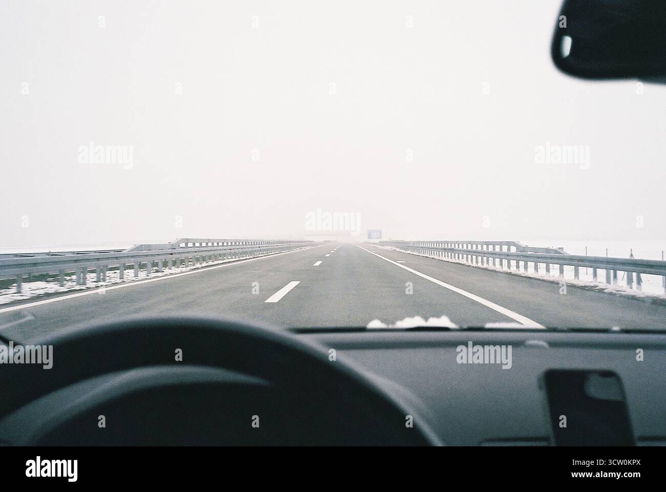 Photo analogique du POV du conducteur montrant une autoroute hivernale vide et sans fin dans un brouillard épais. Neige au sol. Scène de route Moody et atmosphérique. Banque D'Images