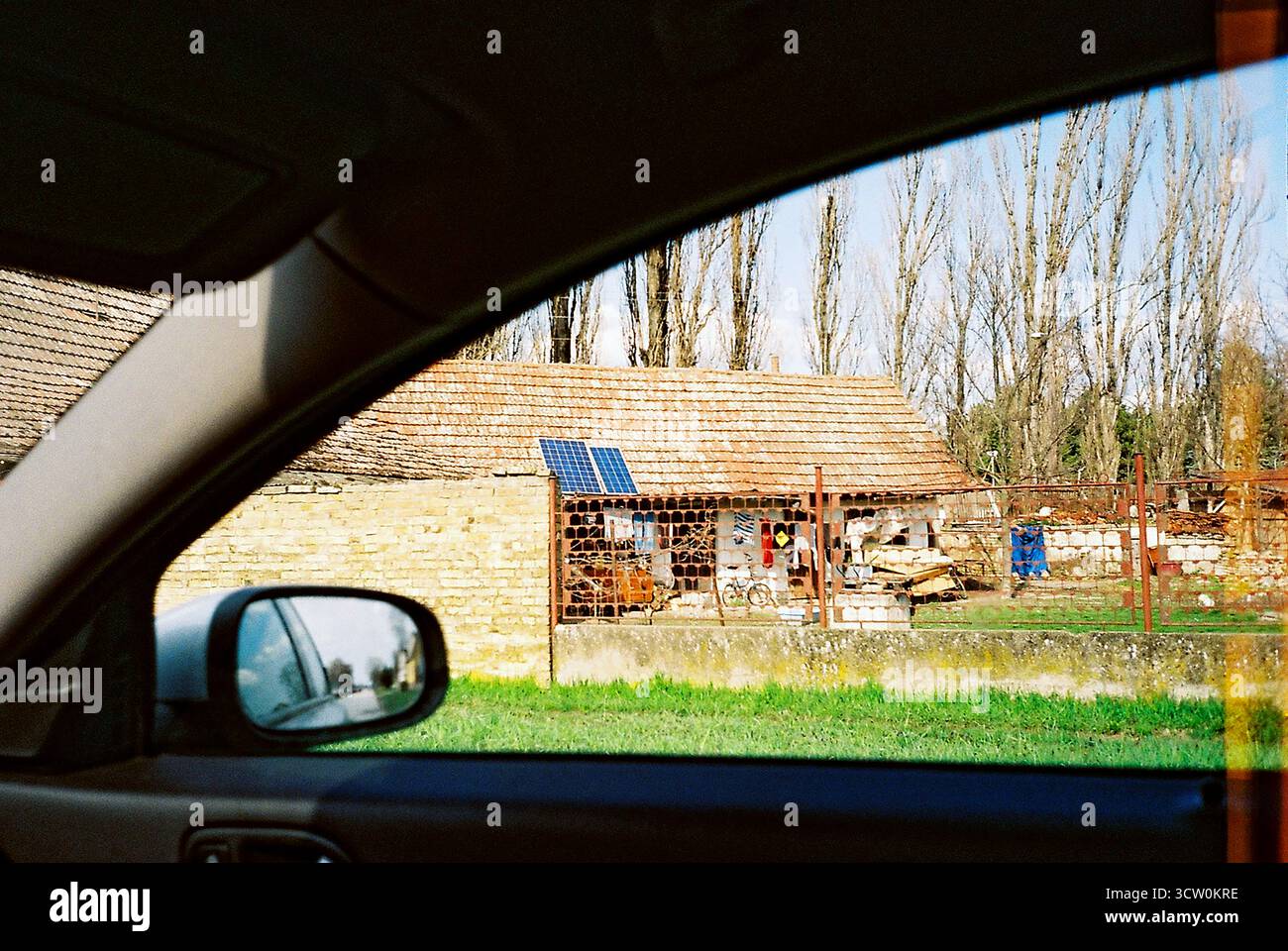 Photo analogique à travers la fenêtre passager d'une maison minable avec deux panneaux solaires sur le toit. Juxtaposition de la décomposition et de l'énergie moderne. Banque D'Images