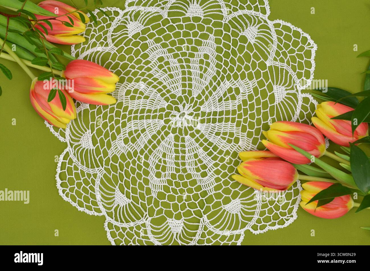 Grand, blanc, rétro, vintage crocheté doily sur fond vert orné de tulipes jaunes et rouges. Décoration féminine. Banque D'Images