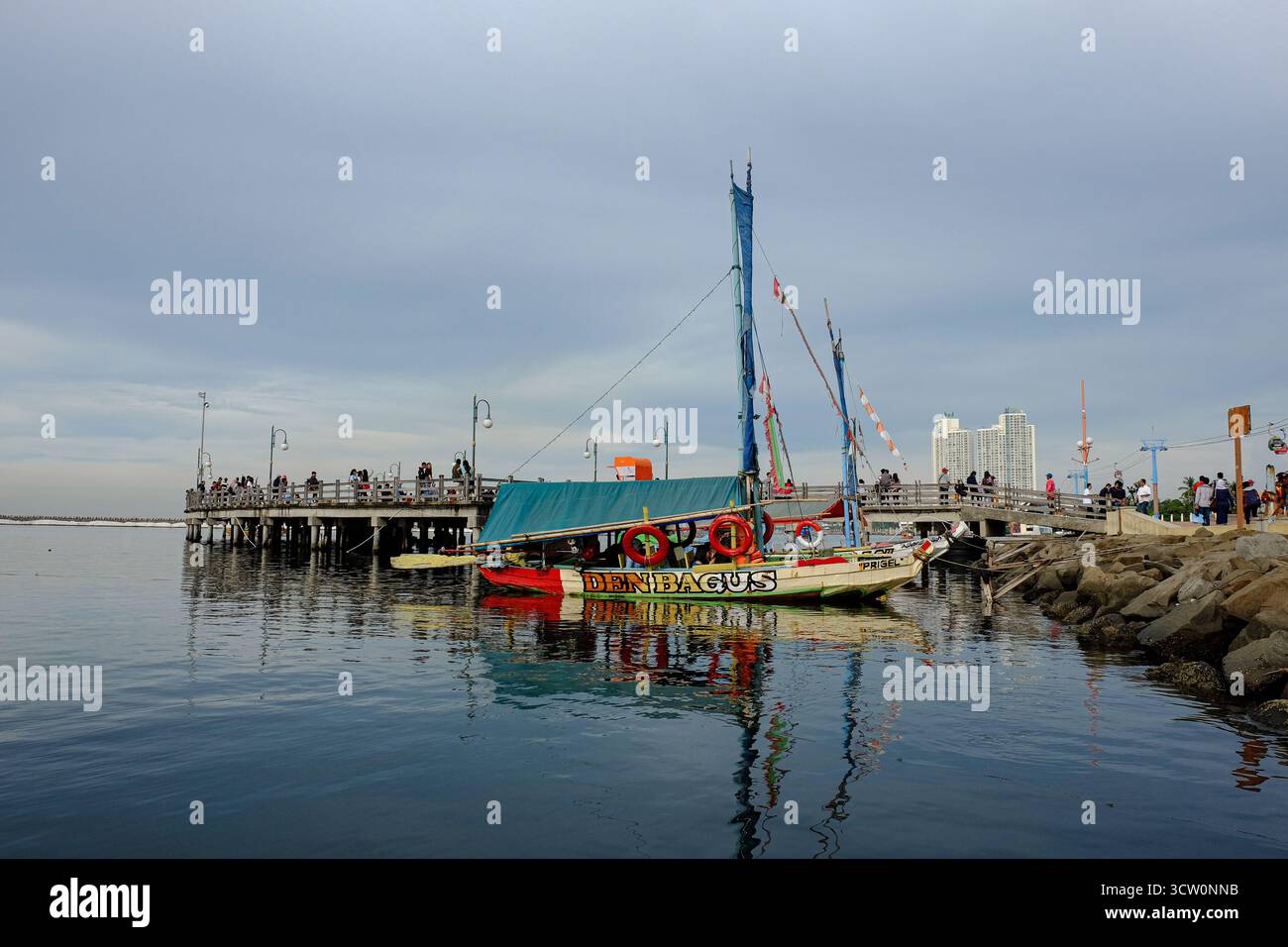 Un bateau traditionnel coloré nommé « Den Bagus » a accosté à Ancol Pier, au nord de Jakarta. Les habitants apprécient le calme front de mer par un après-midi nuageux Banque D'Images