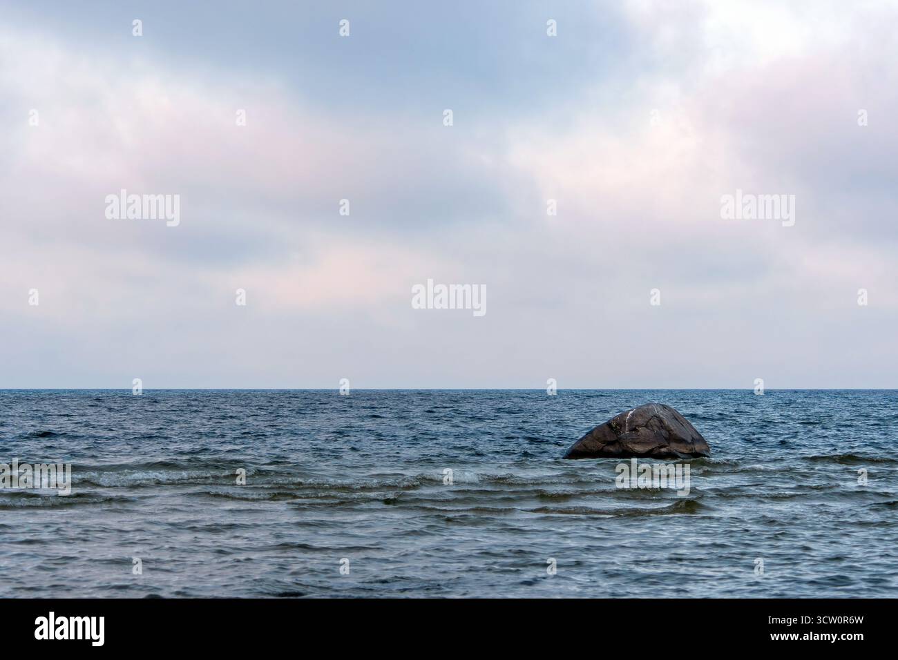 Un rocher solitaire dépasse des eaux calmes de la mer Baltique sous un ciel couvert. Banque D'Images