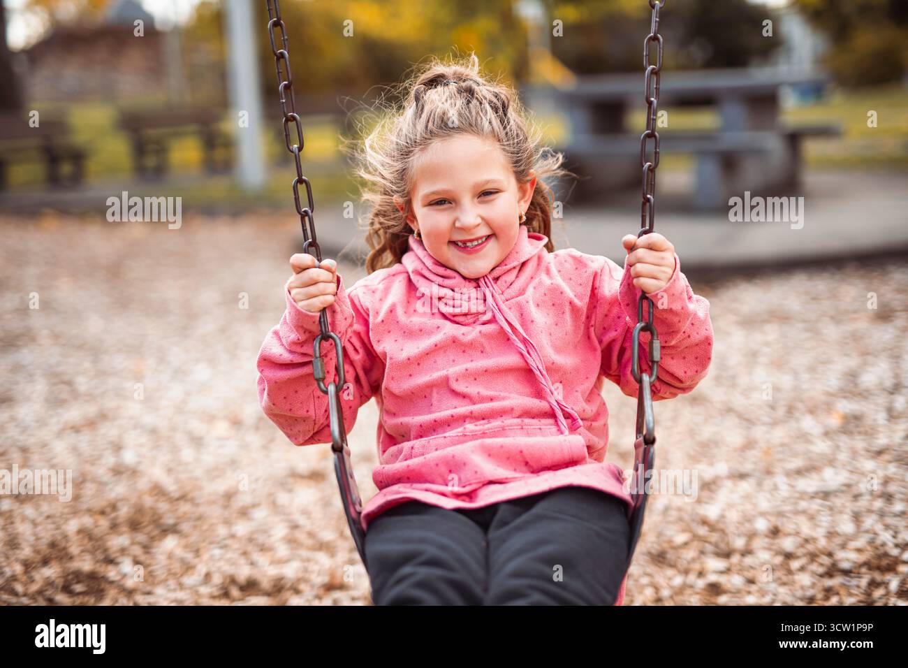 Une petite fille s'amusant sur une aire de jeux dans un parc public le jour d'automne. Banque D'Images