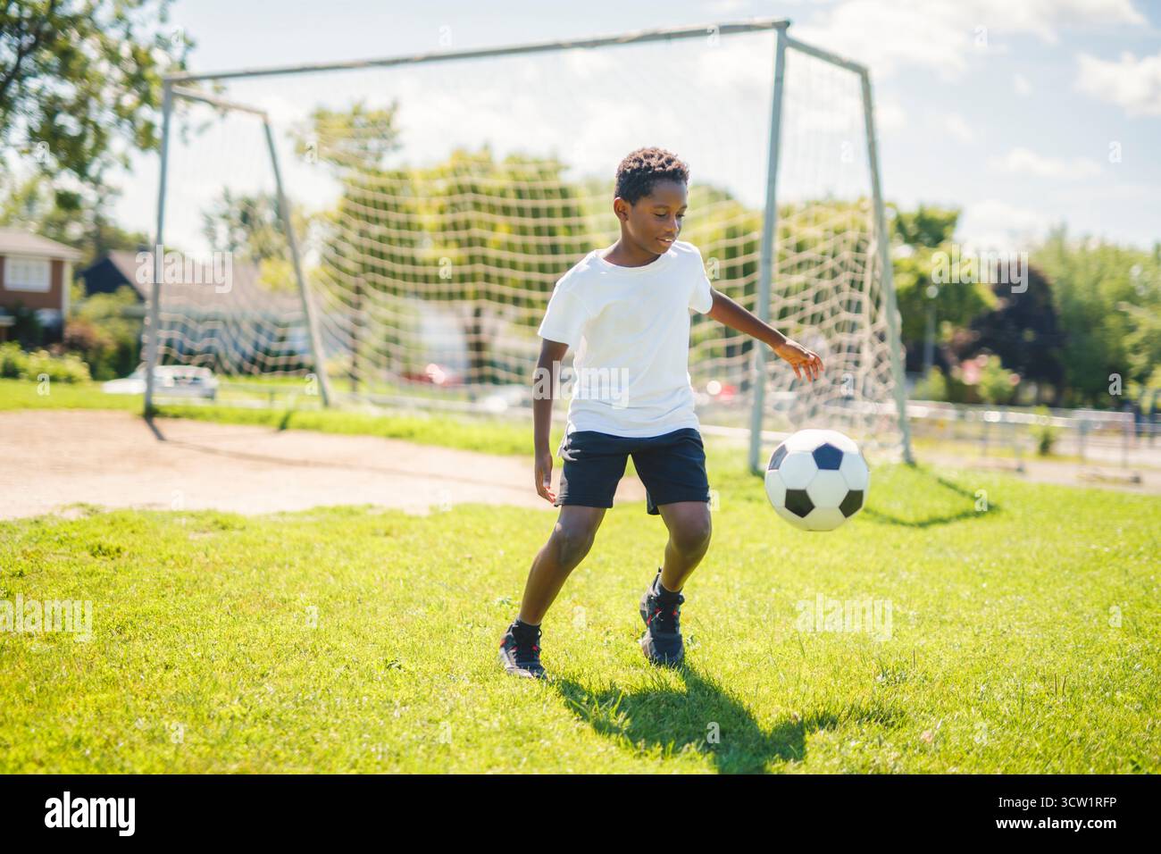 Un jeune enfant jouant au football sur un terrain de jeu Banque D'Images
