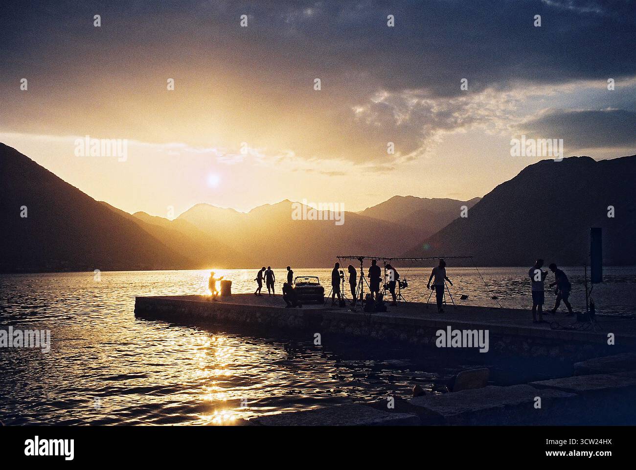 L'équipe de tournage se rassemble après le tournage sur un quai de béton au coucher du soleil dans la baie de Kotor, Monténégro. Photo de film analogique 35mm avec reflet de mer et silhouettes. Banque D'Images