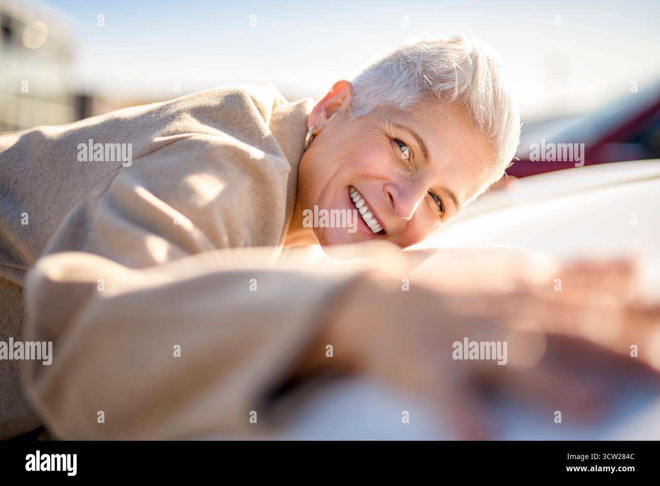 Un heureux propriétaire. Belle femme mature assise détendue dans sa voiture nouvellement achetée. Banque D'Images