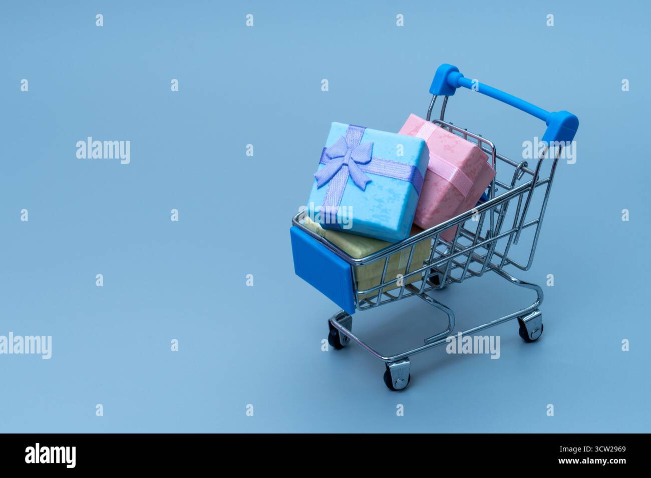 Mini panier rempli de boîtes cadeaux colorées sur fond bleu. Achat en ligne, vente au détail, ventes de vacances et concept d'achat de consommateurs. Copier Banque D'Images