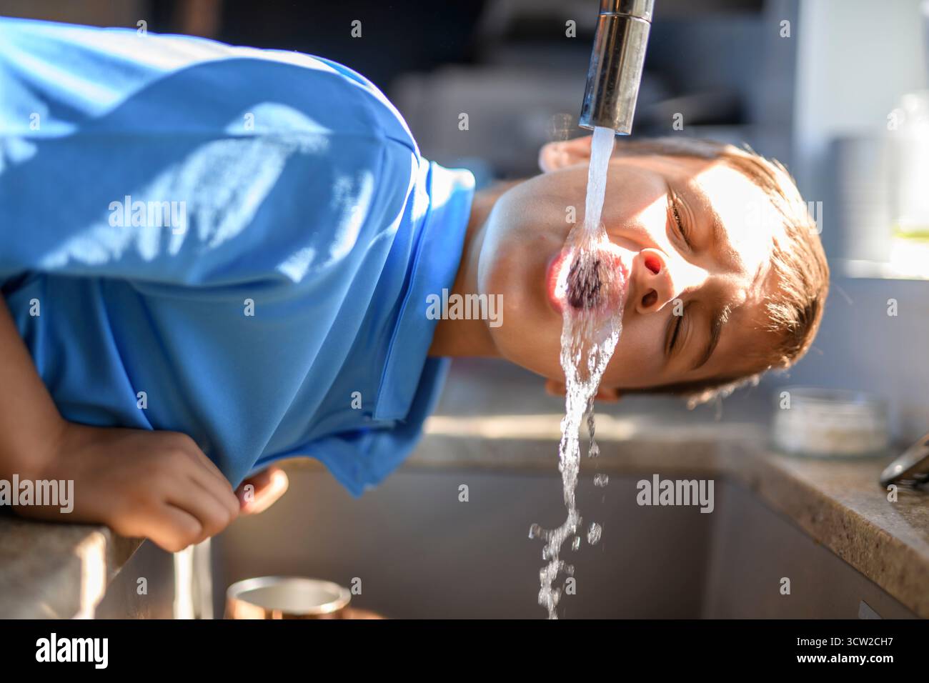 Un garçon buvant de l'eau directement du robinet Banque D'Images
