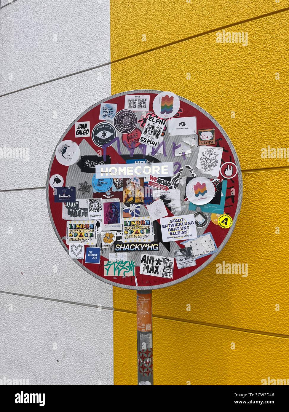 Panneau d'arrêt urbain recouvert d'autocollants colorés sur un fond jaune et blanc éclatant. Street art et culture urbaine capturés de manière audacieuse. - Image de stock capturée avec un smartphone